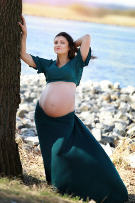 kobieta w ciąży przy drzewie pozująca w zielonej sukni